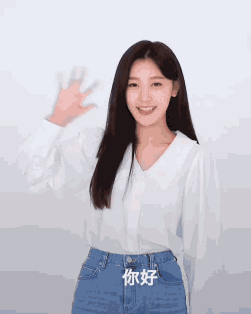 a woman wearing a white shirt and blue jeans is waving
