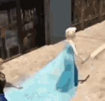 a doll in a blue dress is standing on a sidewalk .