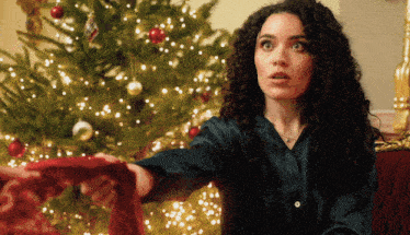 a woman in front of a christmas tree is holding a red scarf
