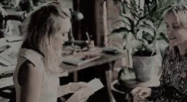 two women are sitting at a table talking to each other .