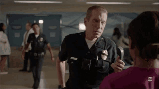 a man in a police uniform is talking to a woman in a pink shirt with abc written on it