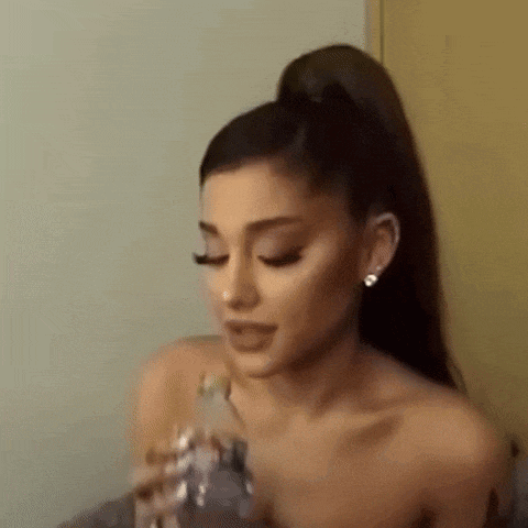 ariana grande is holding a bottle of water in her hand and drinking it .
