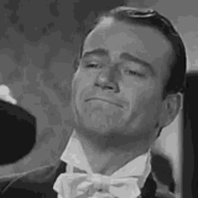 a black and white photo of a man wearing a tuxedo and bow tie .