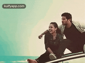 a man and a woman are sitting on the roof of a car next to the ocean .