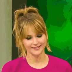 a woman in a pink shirt is smiling with a green background behind her