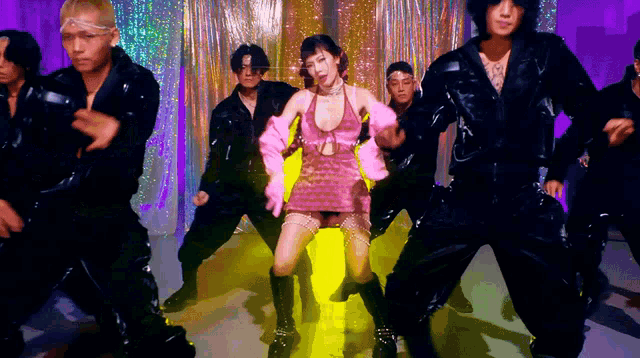 a woman in a pink dress is surrounded by men