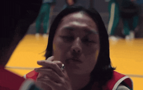 a man with long hair is smoking a cigarette in a gym while another man looks on .