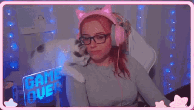 a woman wearing headphones is holding a cat on her shoulder .