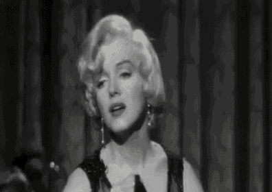 a black and white photo of marilyn monroe holding a glass of wine in her hands .