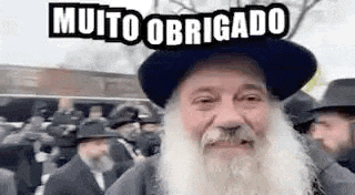 a man with a beard is wearing a hat and smiling in front of a crowd .