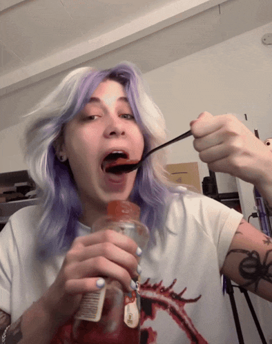 a girl with purple hair is eating ketchup from a bottle