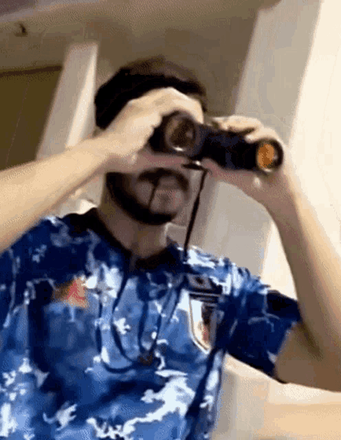 a man wearing a blue shirt is looking through binoculars