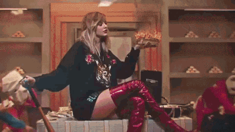 a woman wearing red over the knee boots and a black sweater is sitting on a table holding a piece of pizza .