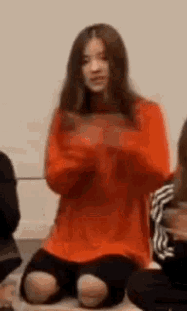 a woman in an orange sweater is sitting on the floor .