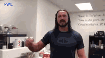 a man with long hair and a beard is standing in front of a wall that says pwic