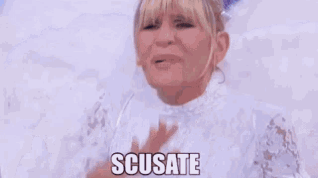 a woman in a white dress is sitting on a bed with feathers on her wings and says scusate .