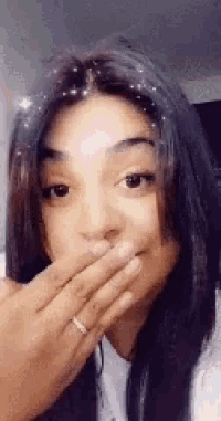 a woman is covering her mouth with her hand while wearing a ring .