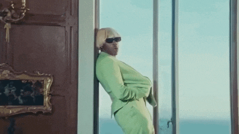 a man in a green suit and sunglasses is leaning against a wall in a room .
