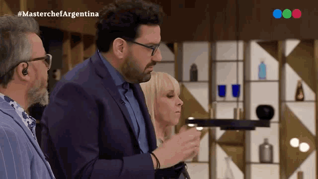 a man in a purple suit stands in front of a woman and a sign that says masterchef argentina on the bottom