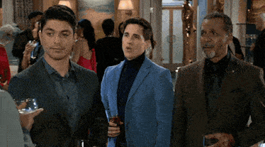 three men in suits are standing in a room with a woman in a red dress