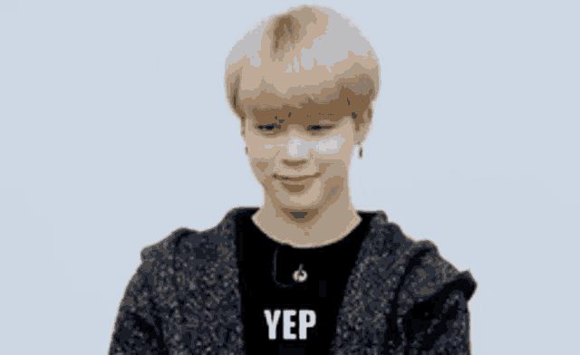 a young man with blonde hair is wearing a black shirt and a gray sweater and says yep .