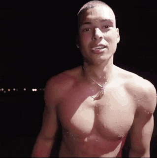 a shirtless man with a necklace around his neck is standing in the dark