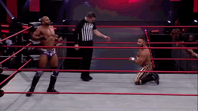a wrestler kneeling down in a ring with a referee standing behind him