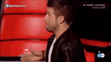 a man in a black leather jacket is standing in front of a red couch .
