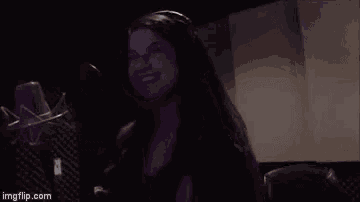 a woman is singing into a microphone in a recording studio and smiling .