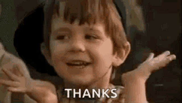 a little boy is smiling and giving a thanks sign .