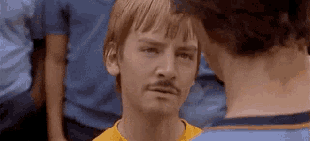 a man with a mustache is standing next to another man in a crowd of people .