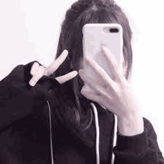 a girl in a black hoodie is taking a selfie with her phone .