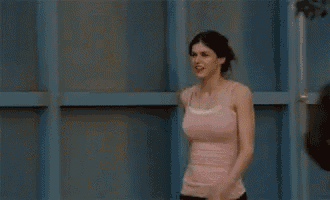 a woman in a pink tank top is standing in front of a building .