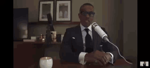 a man in a suit and tie is sitting at a desk in front of a microphone
