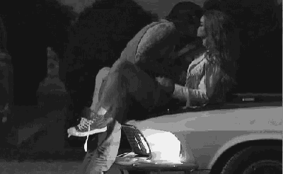 a black and white photo of a man and a woman kissing in the back of a car .
