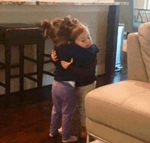 two little girls hugging each other in a living room next to a couch