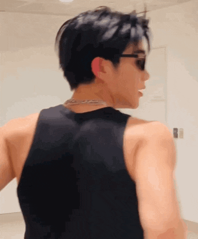 a man wearing sunglasses and a black tank top is standing in front of a white wall .