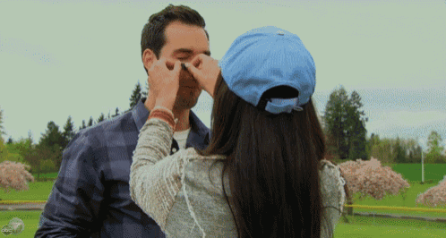 a woman in a blue hat is touching a man 's nose