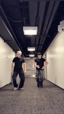 two men are dancing in a hallway with an exit sign on the wall