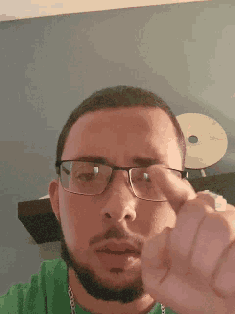 a man wearing glasses and a green shirt is giving a thumbs down sign