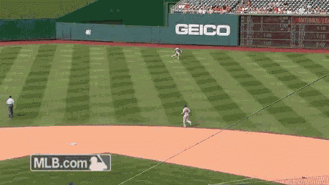 a baseball game is being played in front of a green geico sign