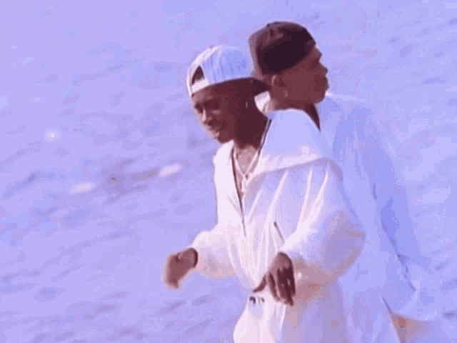 two men in white jumpsuits and hats are walking on the beach .