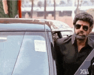 a man wearing sunglasses is getting out of a black car .