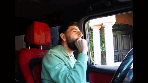 a man with a beard is sitting in a car with his eyes closed