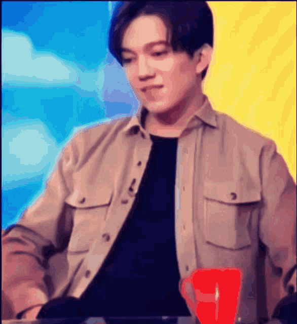 a man in a tan shirt sits in front of a red cup