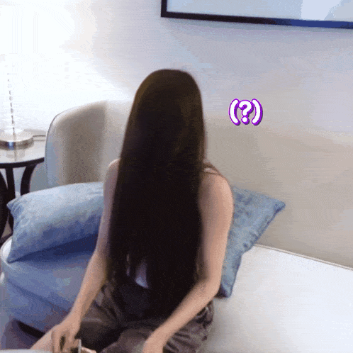a woman with long black hair is sitting on a couch with a purple question mark on her forehead