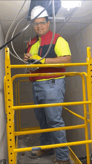 a man standing on a yellow scaffolding looking at wires
