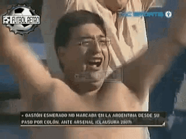 a shirtless man is screaming with his arms in the air while watching a soccer match .