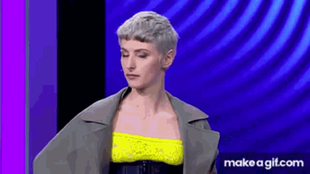 a woman with short hair and a yellow top is standing in front of a blue background .