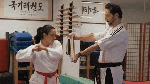 a man and a woman are practicing martial arts in front of a wall with korean writing